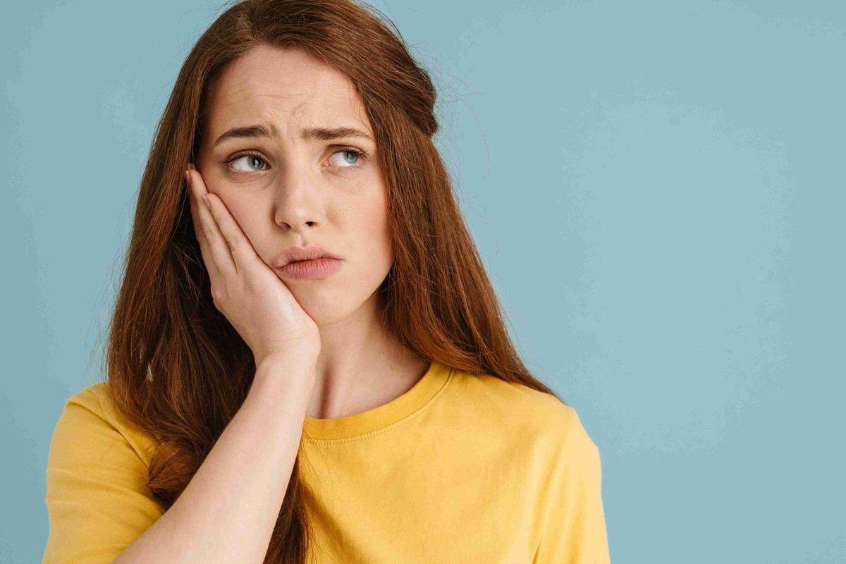 Woman holding her cheek due to sudden dental pain requiring urgent care